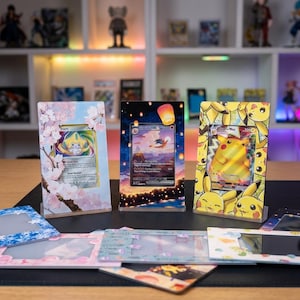 May include: Three vertical acrylic display frames holding trading cards. The left frame features pink cherry blossoms, the center frame shows a night sky with floating lanterns, and the right frame displays a yellow Pikachu pattern.