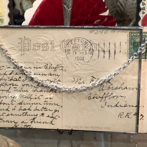 May include: A vintage postcard with a silver chain attached to it. The postcard is addressed to Mr. Flood Abraham in Bluffton, Indiana. The postcard is dated 1909 and has a handwritten message that reads "Bet I am in Bluffton and have seen any body that I know yet. Suppose you have a good time. Thanks. Giving. Well it is about dinner time and I had better get something to eat from a friend. A little"