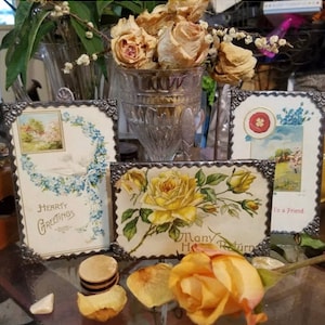 May include: Three vintage postcards with decorative silver frames. The postcards feature images of flowers, a dove, and a house. The text on the postcards reads "Hearty Greetings" and "To a Friend".