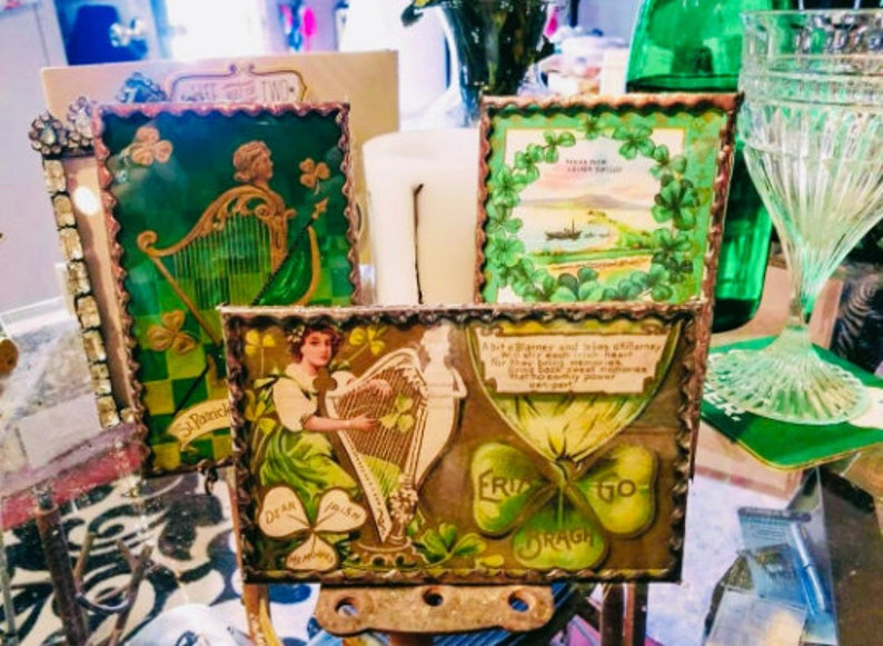 May include: Four vintage picture frames with green, gold, and white accents. The frames feature images of a harp, shamrocks, and a quote about Irish blessings. The frames are displayed on a table with a green tablecloth.