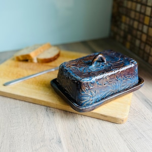 Handmade ceramic butter dish with lid, embossed flower pattern, sapphire blue glaze, placed on a wooden board