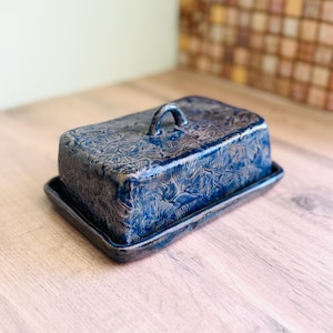May include: A rectangular ceramic butter dish with a deep blue glaze and a textured ginkgo leaf pattern. The lid features a small arched handle, and the base has a matching blue finish with dark edges, creating a cohesive look for the kitchen.