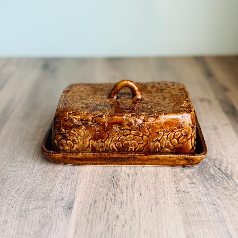 Handmade ceramic butter dish with lid, embossed flower pattern, GLOSSY GOLD CARAMEL glaze, placed on a wooden board
