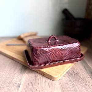 Handmade ceramic butter dish with lid, embossed flower pattern, RUSTIC PURPLE PINK glaze, placed on a wooden board