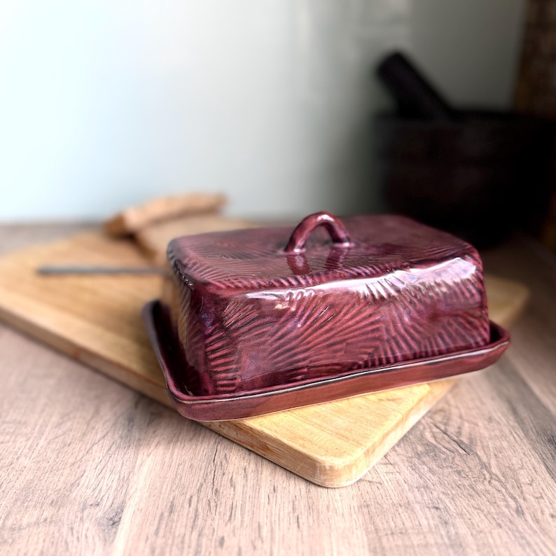 Handmade ceramic butter dish with lid, embossed flower pattern, RUSTIC PURPLE PINK glaze, placed on a wooden board
