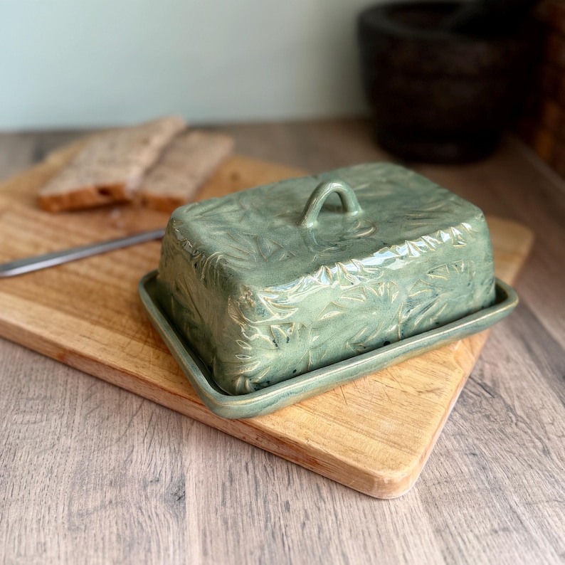 Handmade ceramic butter dish with lid, embossed flower pattern, GRASS GREEN glaze, placed on a wooden board