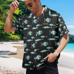 May include: Black short-sleeved shirt featuring a repeating pattern of blue fish and bubbles. The shirt has a classic collar. The word "Metlox" is printed on the shirt. The shirt is worn on a beach.