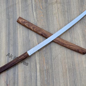 Op de afbeelding: Een katana-zwaard met een gepolijst zilveren lemmet en een donkerhouten handvat en schede. Het handvat en de schede zijn gemaakt van donker hout. De tekst "Ak Knives" staat op het handvat.