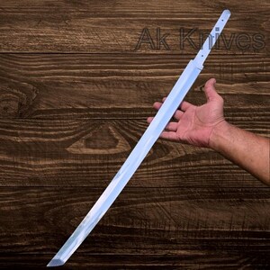 May include: A long, silver-colored sword with a sharp blade. The sword is held in a hand against a dark wood background. The text "Ak Knives" is visible in the upper right corner.