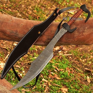 May include: A Damascus steel sword with a curved blade and a leather-wrapped handle. The sword is accompanied by a black leather sheath and a shoulder strap. The text "Ak Knives" is visible on the handle.
