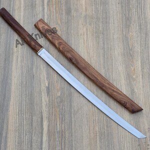 May include: A katana-style sword with a polished steel blade and a dark wood handle and sheath. The text "Ak Knives" is printed on the handle. The sword is displayed on a wooden surface.