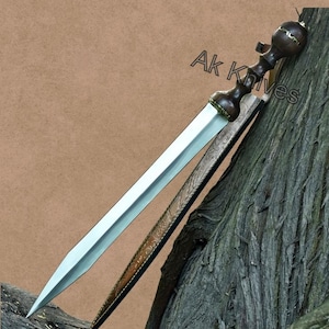 Könnte beinhalten: Ein römisches Gladius-Schwert mit polierter Stahlklinge und dunklem Holzgriff. Das Schwert wird mit seiner Lederscheide präsentiert, die ein geprägtes Design aufweist. Der Text "Ak Knives" ist sichtbar.