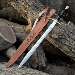 May include: A silver sword with a double-edged blade and a gold-colored crossguard. The black handle is wrapped with a braided design. The sword is in a brown leather sheath with decorative stitching and the text "Ak Knives".