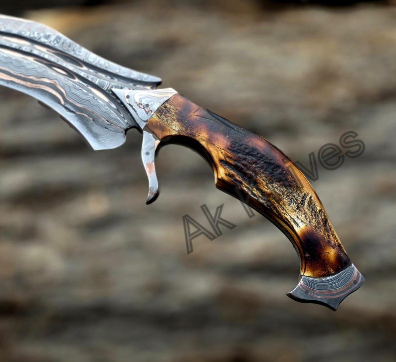 May include: Close-up of a custom-made knife with a curved, patterned blade. The handle is crafted from dark brown material with a unique, textured appearance. The blade has a silver and copper design. The text "Ak Knives" is visible on the handle.