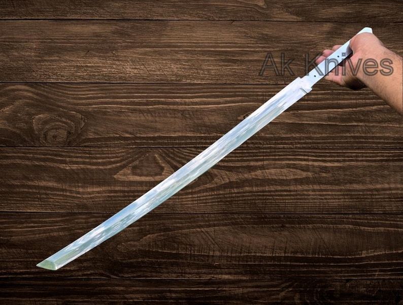 May include: A long, straight sword with a white handle and a reflective blade. The blade has a slight curve and a sharp point. The text "Ak Knives" is visible on the wooden background.
