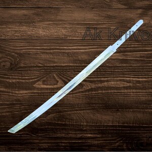May include: A katana blade with a light blue and silver finish, resting on a dark brown wooden surface. The blade has a straight edge and a pointed tip. The text "Ak Knives" is visible in the background.