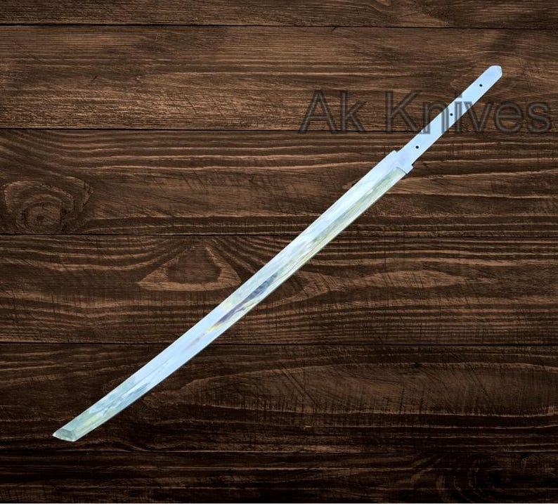 May include: A katana blade with a light blue and silver finish, resting on a dark brown wooden surface. The blade has a straight edge and a pointed tip. The text "Ak Knives" is visible in the background.