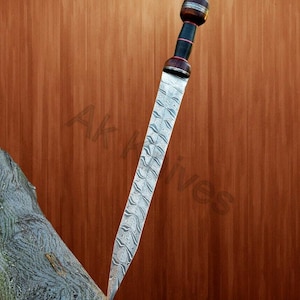Könnte beinhalten: Ein römisches Gladius-Schwert mit gemusterter Klinge und Holzgriff. Der Griff hat einen dunkelbraunen Knauf und einen schwarzen Griff. Die Klinge ist silberfarben mit einem sich wiederholenden Wellenmuster. Das Schwert wird vor einem braunen Holzhintergrund präsentiert.