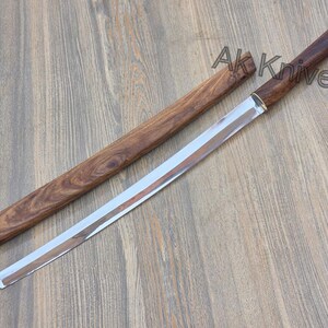 May include: A katana-style sword with a polished steel blade and a wooden handle and sheath. The handle and sheath are a dark brown colour. The text "Ak Knives" is visible on the image.