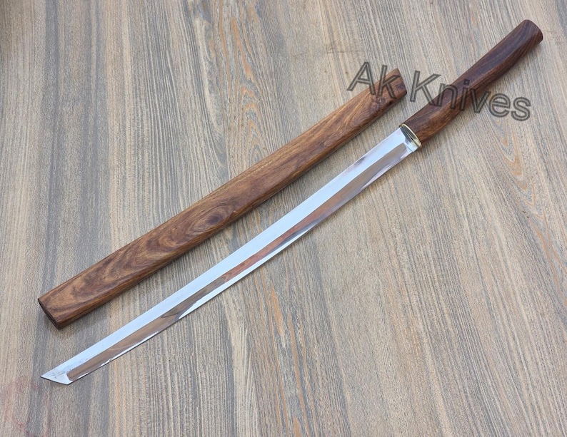 May include: A katana-style sword with a polished steel blade and a wooden handle and sheath. The handle and sheath are a dark brown colour. The text "Ak Knives" is visible on the image.
