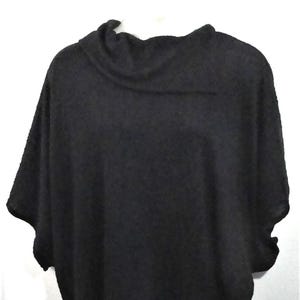 May include: A black poncho-style sweater with a cowl neck. The garment has short sleeves and a scalloped hemline. The sweater is made of a soft, knitted material and is displayed on a white background.