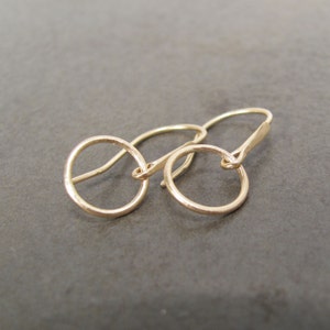 May include: A pair of gold hoop earrings with a simple, minimalist design. The earrings are made of a smooth, polished metal and have a delicate, circular shape.