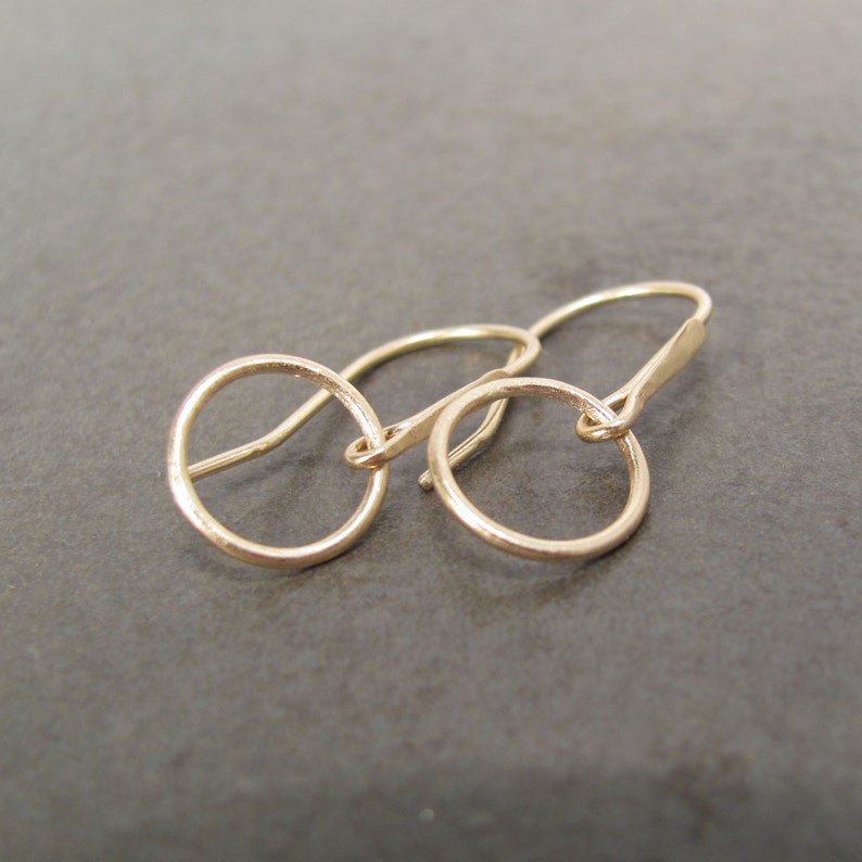May include: A pair of gold hoop earrings with a simple, minimalist design. The earrings are made of a smooth, polished metal and have a delicate, circular shape.