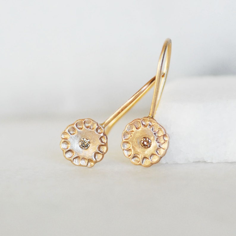 May include: A pair of gold earrings with a small diamond in the center of each earring. The earrings are in the shape of a circle with a textured edge.