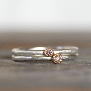 May include: A silver band ring with two small diamonds set in gold. The ring has a hammered texture.