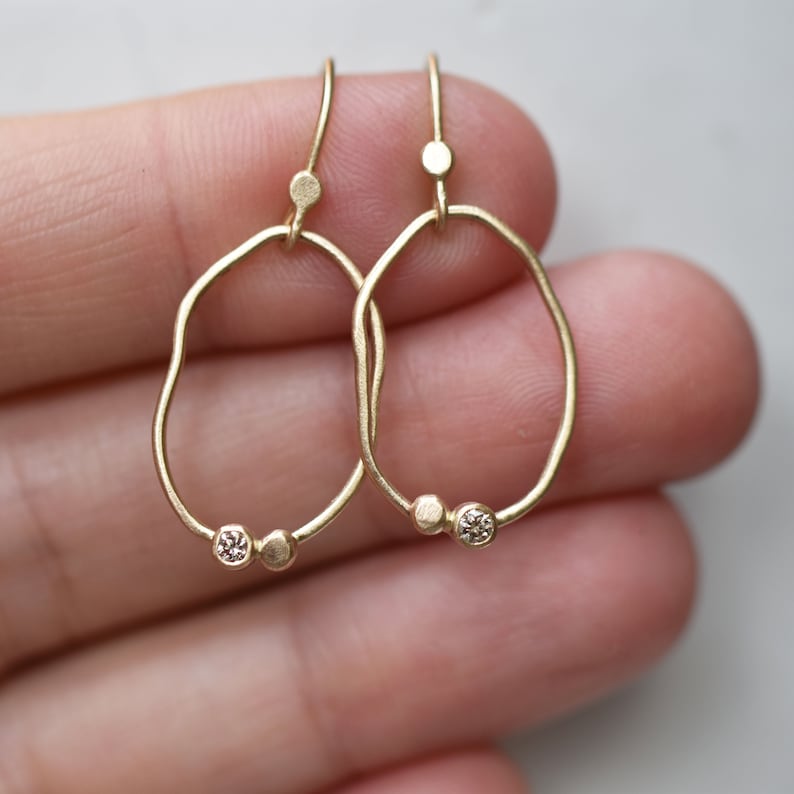 May include: A pair of gold earrings with a unique, organic shape. Each earring features a small, round diamond set in a gold bead.