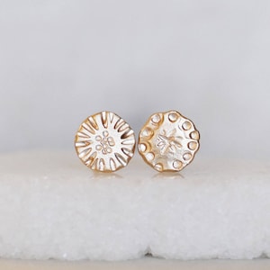 May include: A pair of gold-toned stud earrings with a textured, circular design. Each earring features a different embossed pattern.