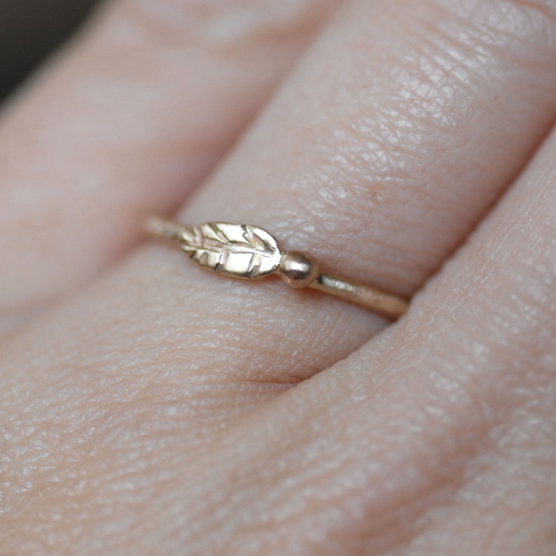 Puede incluir: Un delicado anillo de oro con un peque&ntilde;o dise&ntilde;o de hoja. El anillo se lleva en un dedo.