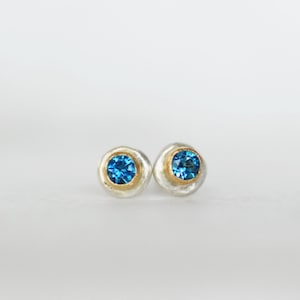 May include: A pair of silver and gold earrings with blue gemstones. The earrings are round and have a textured surface.