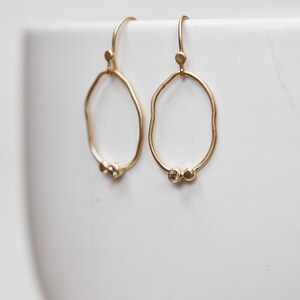 May include: A pair of gold hoop earrings with a textured, irregular shape. Each earring features two small, round, clear gemstones.