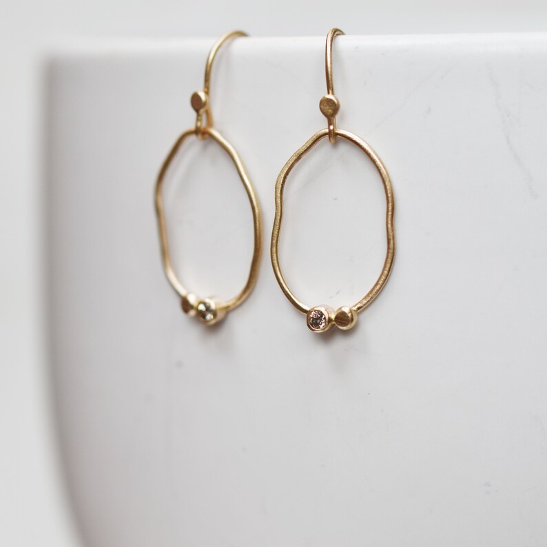 May include: A pair of gold hoop earrings with a textured, irregular shape. Each earring features two small, round, clear gemstones.