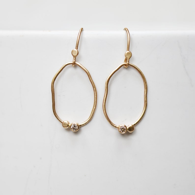 May include: A pair of gold earrings with a unique, organic shape. Each earring features a small, round diamond accent.