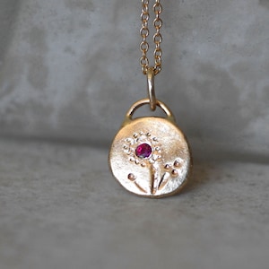 Può includere: Collana d'oro con un ciondolo rotondo che presenta un fiore stilizzato con una pietra preziosa rossa al centro.