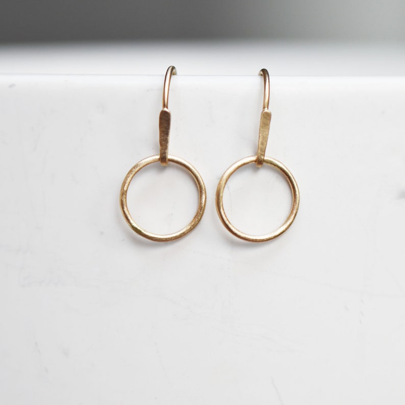 May include: A pair of gold hoop earrings with a simple, minimalist design. The hoops are small and delicate, and they hang from a thin gold wire.