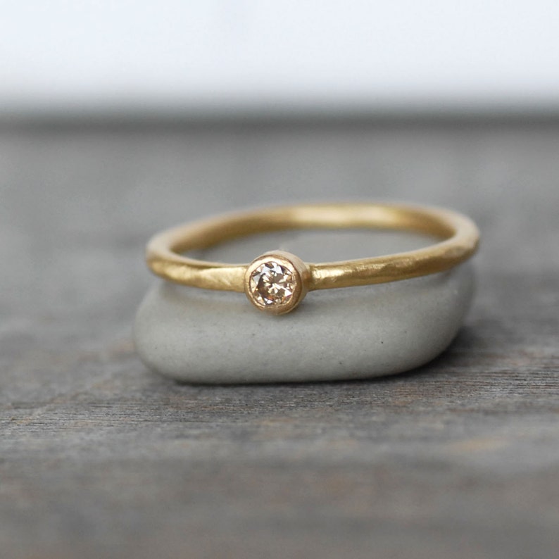 May include: A thin gold band with a single round diamond set in the center. The band has a hammered texture.