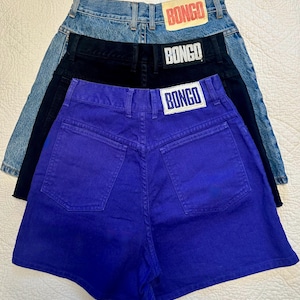 May include: Three pairs of high-waisted denim shorts in blue, black, and purple. Each pair features a back pocket design and a rectangular "BONGO" label at the waistband. The shorts are arranged in a layered composition.
