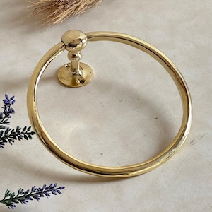 May include: A polished brass towel ring. The circular ring is attached to a wall mount with a ball detail at the top. The design is simple and elegant, suitable for a bathroom. The ring has a diameter of approximately 15 cm.