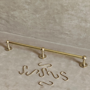 Peut inclure: Un porte-serviettes doré avec des embouts arrondis et un support central, accompagné de plusieurs crochets en forme de S assortis. Le porte-serviettes est conçu pour une utilisation dans la salle de bain et est en métal.