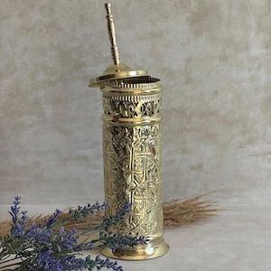 Puede incluir: Un portaescobilla de inodoro dorado y ornamentado, con tapa y asa. El soporte presenta intrincados patrones en relieve y una banda calada decorativa cerca de la parte superior. El mango del cepillo es visible, y el dise&ntilde;o sugiere un estilo vintage o antiguo.