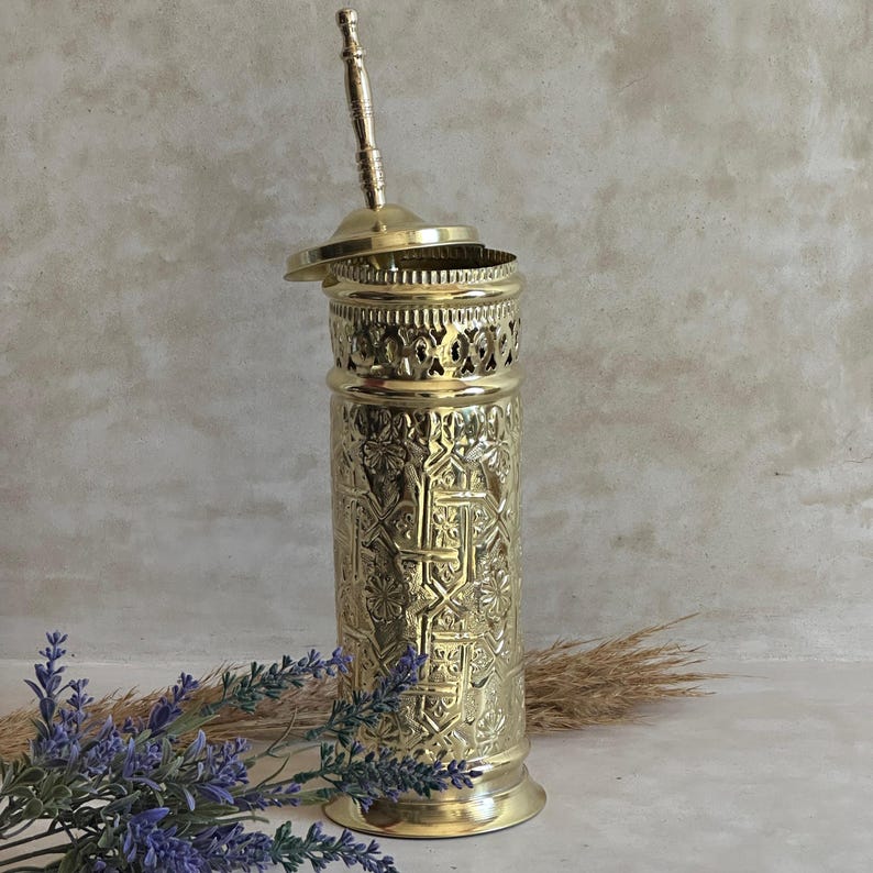 Puede incluir: Un portaescobilla de inodoro dorado y ornamentado, con tapa y asa. El soporte presenta intrincados patrones en relieve y una banda calada decorativa cerca de la parte superior. El mango del cepillo es visible, y el dise&ntilde;o sugiere un estilo vintage o antiguo.