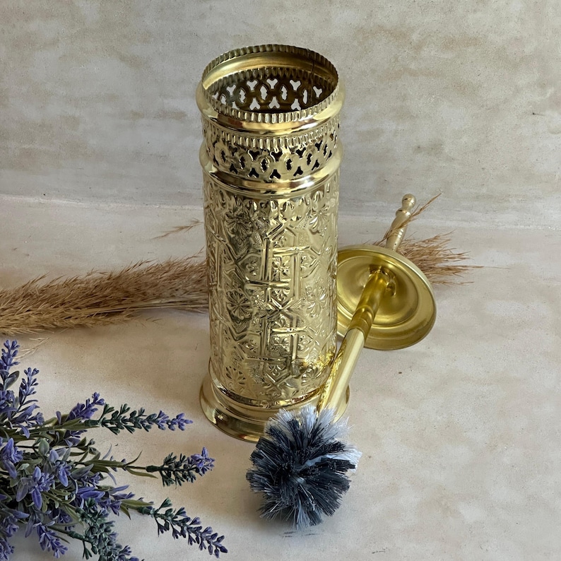 Puede incluir: Un juego de cepillo y soporte para cepillo de inodoro de color dorado. El soporte tiene un patr&oacute;n intrincado y una parte superior calada decorativa. El cepillo tiene un mango dorado y un cabezal de cepillo gris y blanco. El juego est&aacute; dise&ntilde;ado para el ba&ntilde;o.