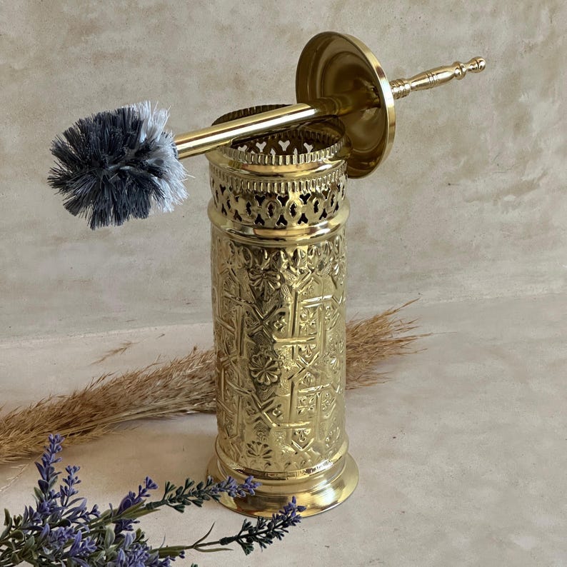 Puede incluir: Un juego de cepillo y soporte para inodoro de color dorado. El soporte tiene un dise&ntilde;o en relieve ornamentado y una parte superior calada decorativa. El cabezal del cepillo tiene cerdas grises y blancas. El juego es para el ba&ntilde;o.