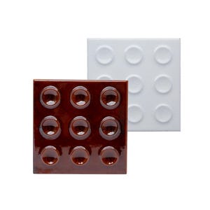May include: Two square tiles, one brown and one white, each with nine raised, circular bumps. The brown tile has a glossy finish, while the white tile has a matte finish. The tiles are likely decorative or functional.