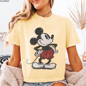 K&ouml;nnte beinhalten: Hellgelbes T-Shirt mit einer Mickey Mouse-Grafik. Die Cartoonfigur ist in Schwarz, Wei&szlig; und Rot gehalten, im Vintage-Skizzenstil. Das Shirt hat kurze &Auml;rmel und einen Rundhalsausschnitt.
