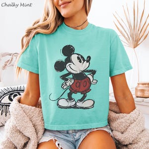 K&ouml;nnte beinhalten: T&uuml;rkisfarbenes T-Shirt mit einem verblichenen Mickey Mouse-Motiv. Die Cartoonfigur ist in Schwarz, Wei&szlig; und Rot dargestellt. Der Text "Chalky Mint" befindet sich oben links. Das Shirt hat kurze &Auml;rmel.