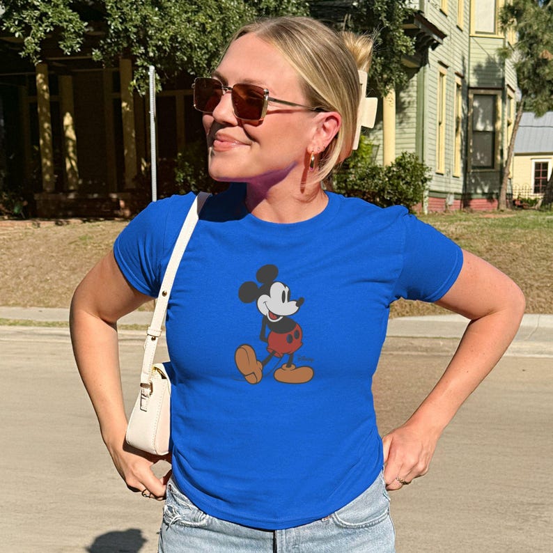May include: A royal blue t-shirt with a classic Mickey Mouse graphic. The cartoon character is shown in his iconic pose, with red shorts, brown shoes, and white gloves. The shirt has a crew neck.
